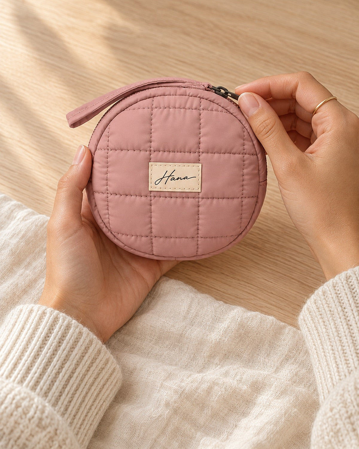 Hands holding the small round quilted Hana pouch, fingers on the zip